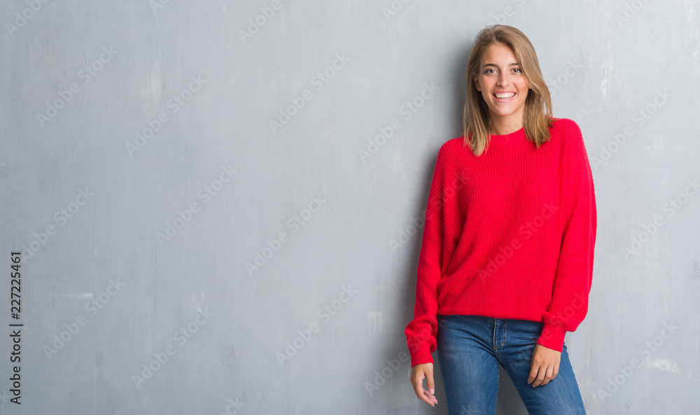 Beautiful young woman standing over grunge grey wall wearing winter sweater with a happy face standing and smiling with a confident smile showing teeth Beautiful young woman standing over grunge grey wall wearing winter sweater with a happy face standing and smiling with a confident smile showing teeth