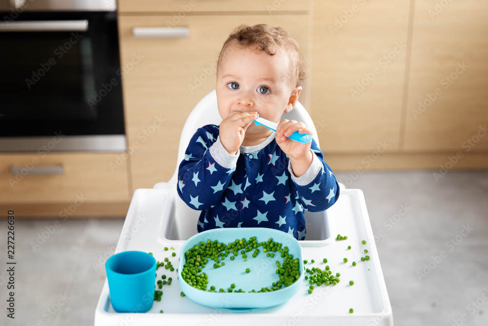 Baby in high chair eating peas with spoon Stock Photo Adobe Stock