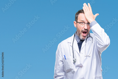 Obraz na płótnie Middle age senior hoary doctor man wearing medical uniform isolated background surprised with hand on head for mistake, remember error