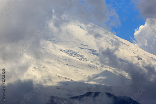The western peak of Mount Elbrus, the slope with snow is visible through the clouds. Mountain range in the North Caucasus in Russia. © olgapkurguzova