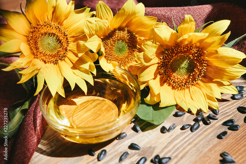 Sunflower oil with yellow flowers with black seeds on wooden background with sunshine