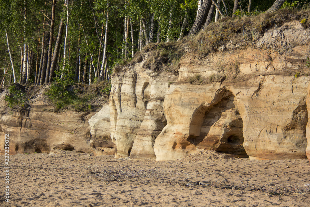 Veczemju Clifs Red Rocks, Latvia. Baltic Sea With Waves, Rocks and Blue Sky Sunny Day. Veczemju Clifs Red Rocks, Latvia. Baltic Sea With Waves, Rocks and Blue Sky Sunny Day.