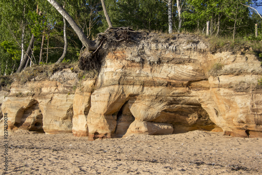 Veczemju Clifs Red Rocks, Latvia. Baltic Sea With Waves, Rocks and Blue Sky Sunny Day. Veczemju Clifs Red Rocks, Latvia. Baltic Sea With Waves, Rocks and Blue Sky Sunny Day.