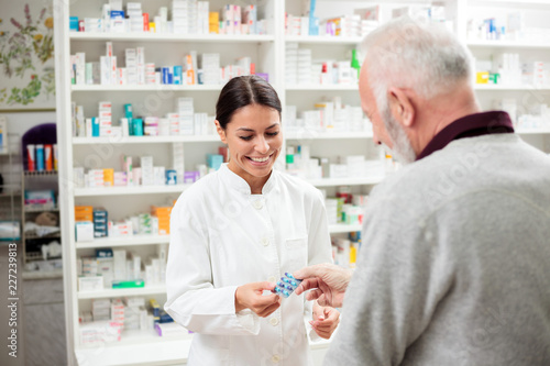 Medicine, pharmaceutics, health care and people concept - happy pharmacist giving medications to senior man customer