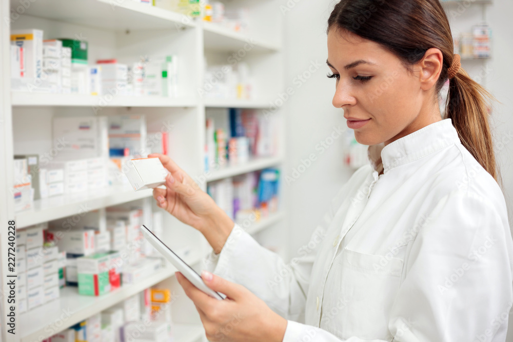 Medicine, pharmaceutics, health care and people concept - Serious young female pharmacist taking medications from the shelf.