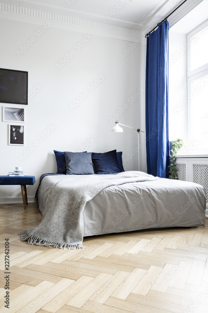 Low angle view of a cozy double bed in a corner of a bright bedroom interior with navy blue textiles and herringbone parquet floor - obrazy, fototapety, plakaty 