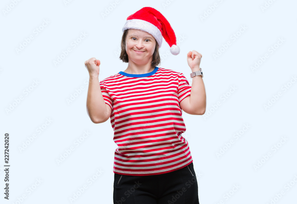 Young adult woman with down syndrome wearing christmas hat over isolated background very happy and excited doing winner gesture with arms raised, smiling and screaming for success. Celebration Young adult woman with down syndrome wearing christmas hat over isolated background very happy and excited doing winner gesture with arms raised, smiling and screaming for success. Celebration