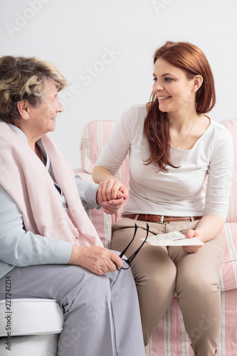 Fotografie Happy caregiver talking with smiling senior woman while visit her at nursing hou