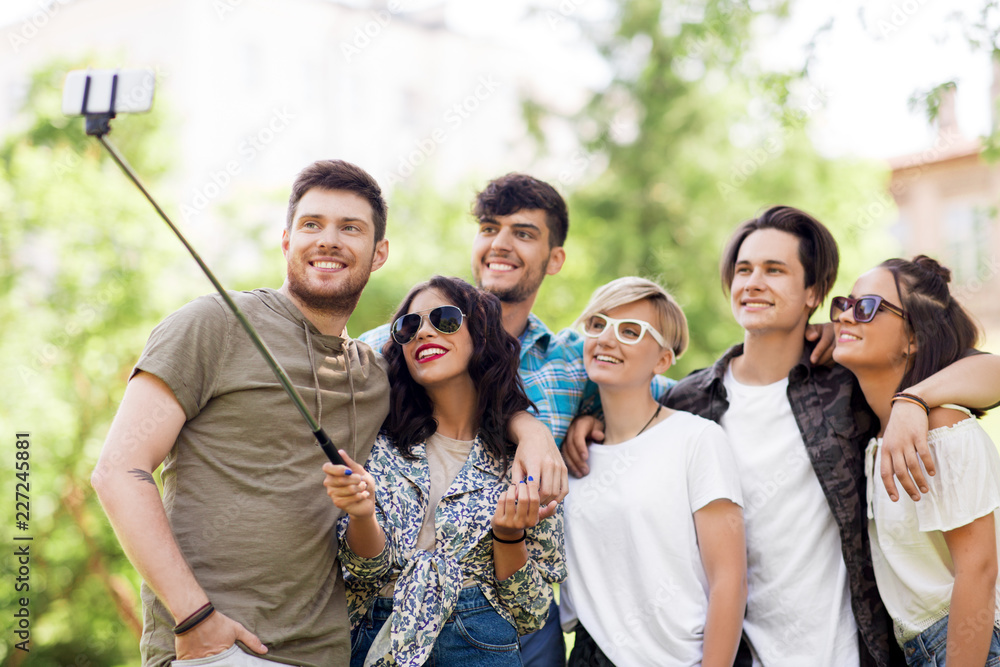 friendship, leisure and technology concept - group of happy smiling friends taking picture by selfie stick at summer park friendship, leisure and technology concept - group of happy smiling friends taking picture by selfie stick at summer park