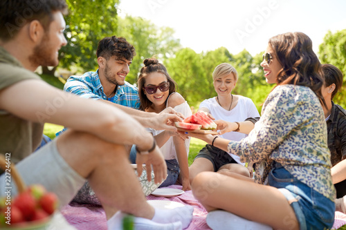 friendship, leisure and food concept - group of happy friends sharing watermelon at picnic in summer park