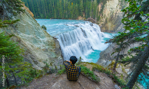 A man sitting on a ground looking at Wapta falls in Canada