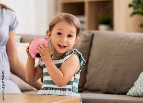 фотографія savings and finances concept - happy little girl with piggy bank at home