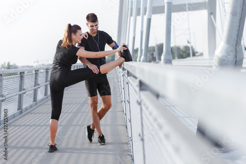 Young couple doing morning workout outdoors. Young man and woman stretching they muscle before running on bridge.