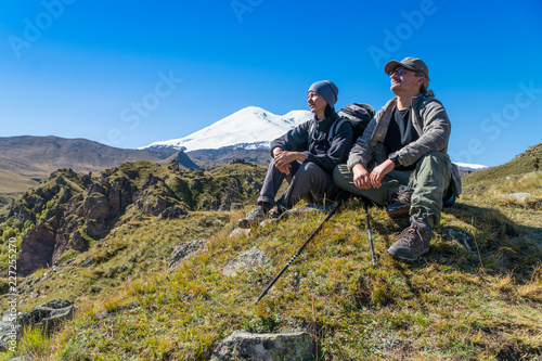 Man and woman with backpack admiring Elbrus mountain view landscape from the cliff edge. Enjoying nature vacation travel adventure at Caucasus mountains.