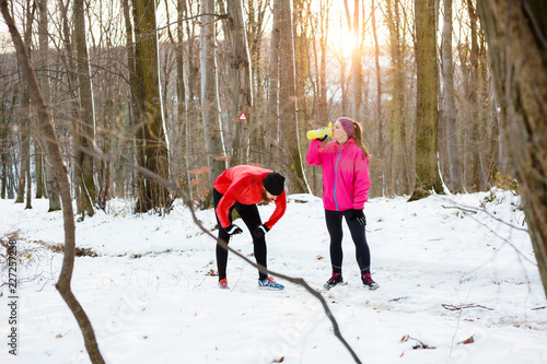 Tired young couple relaxing and hidrating after a workout in a snow covered forest. Active and healthy lifestyle concept. photo