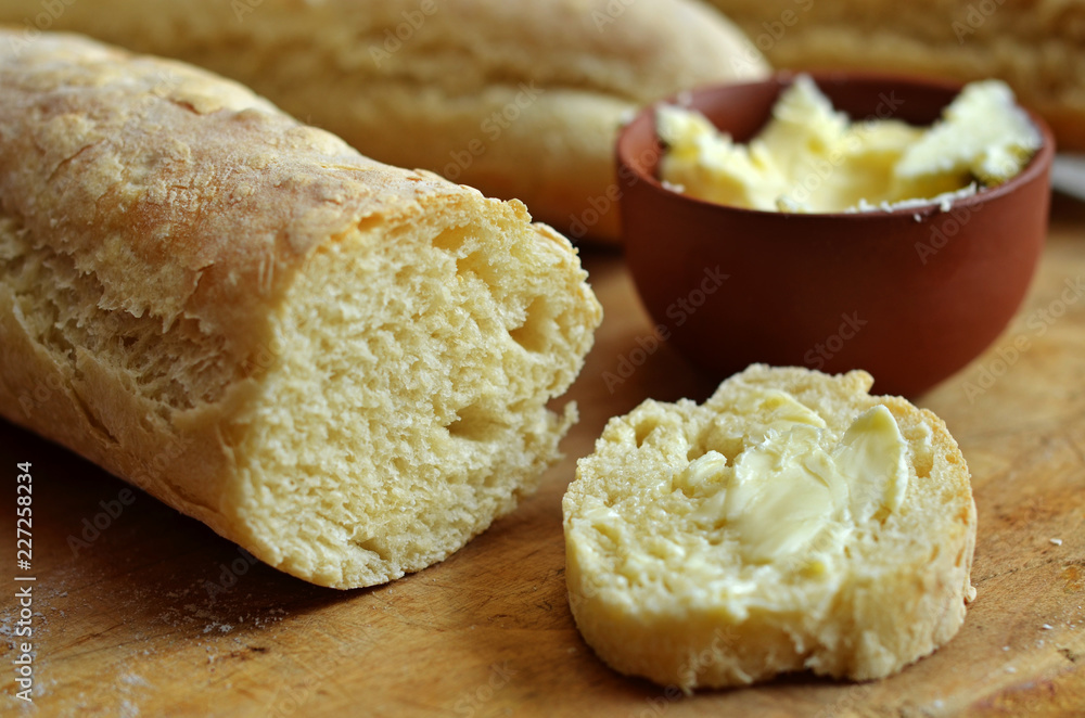A baguette spread with butter on a wooden board A baguette spread with butter on a wooden board