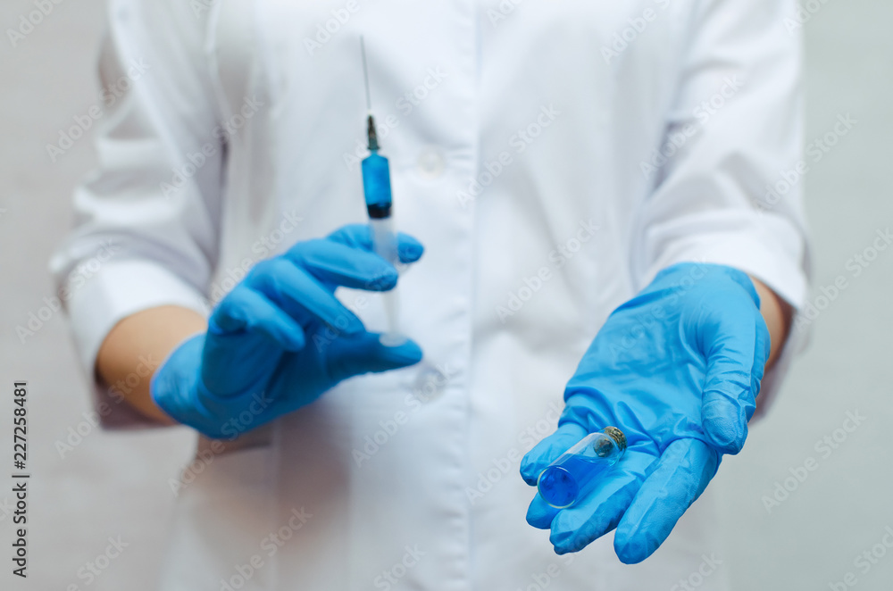 Syringe with a blue medical drug in the doctor hands dressed in the medical gown.