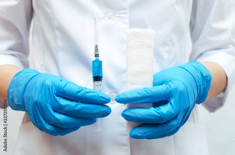 Syringe with a blue medical drug and a bandage in the doctor hands dressed in the medical gown. Syringe with a blue medical drug and a bandage in the doctor hands dressed in the medical gown.