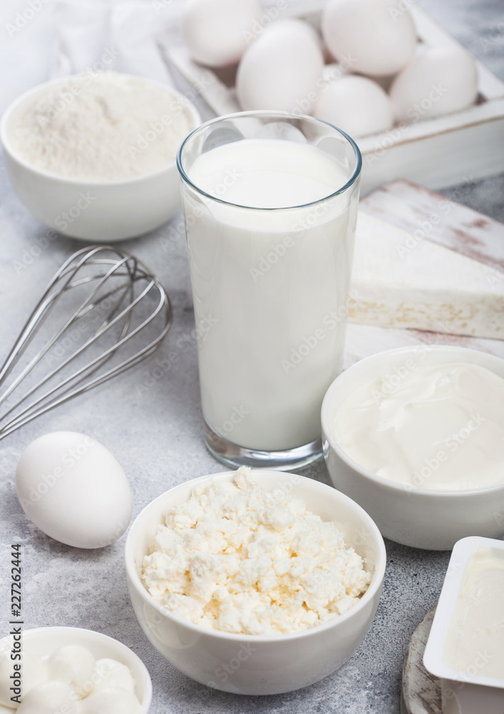 Fresh dairy products on white table background. Glass of milk, bowl of sour cream and cottage cheese and eggs in wooden box. Steel whisk. Fresh dairy products on white table background. Glass of milk, bowl of sour cream and cottage cheese and eggs in wooden box. Steel whisk.