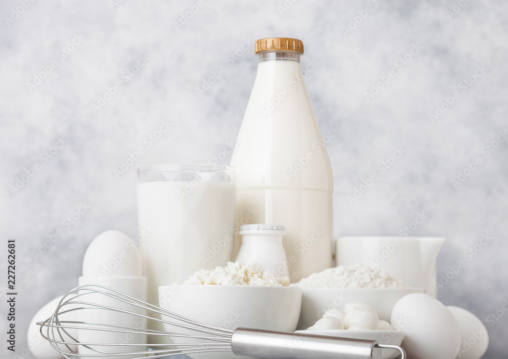 Fresh dairy products on white table background. Plastic bottle and glass of milk, bowl of cottage cheese and baking flour and mozzarella. Eggs and cheese. Steel whisk. Fresh dairy products on white table background. Plastic bottle and glass of milk, bowl of cottage cheese and baking flour and mozzarella. Eggs and cheese. Steel whisk.