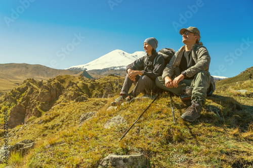 Man and woman with backpack admiring Elbrus mountain view landscape from the cliff edge. Enjoying nature vacation travel adventure at Caucasus mountains.