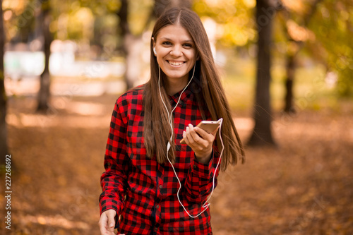 Pretty girl holding phone and listening music with her headphones in autumn