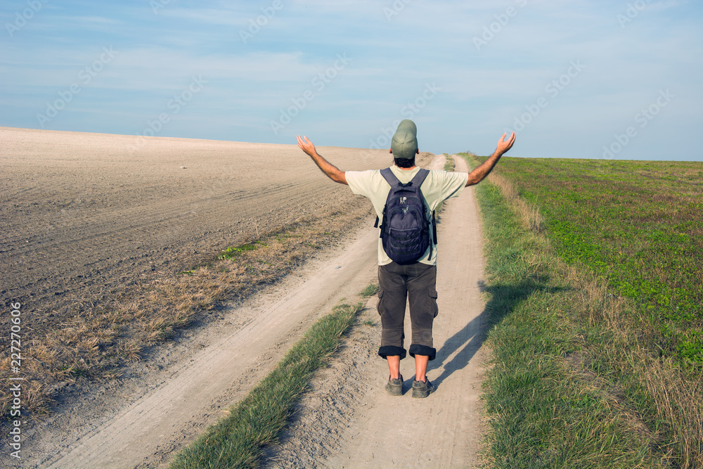 Fototapeta premium Man traveler on a dirt road with hands up