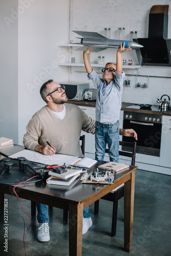adorable son holding rocket model at table at home