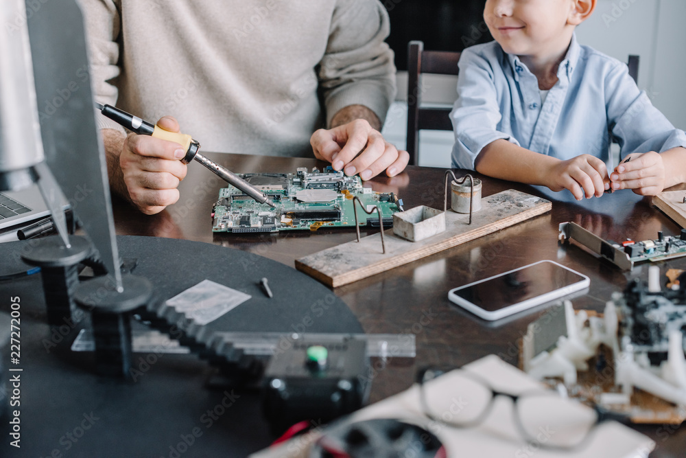 cropped image of father and son soldering circuit board with soldering iron at home