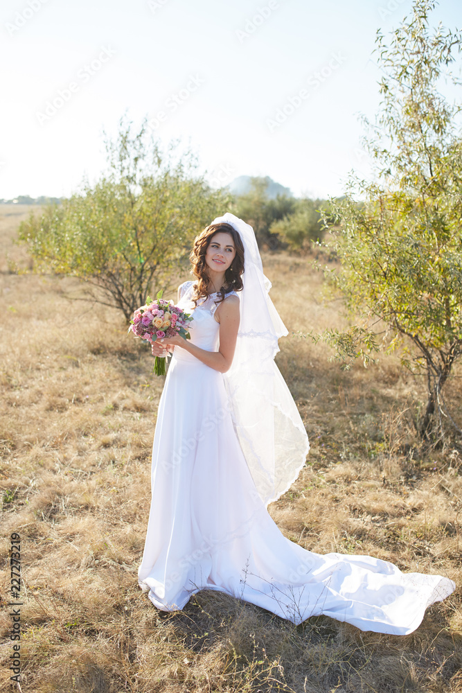 Beautiful smiling bride wearing a natural flower wreath and standing in the golden summer fields