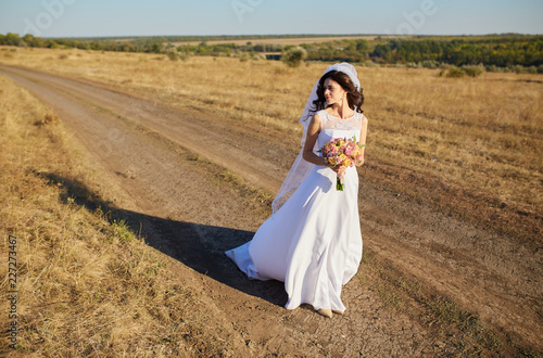 Beautiful smiling bride wearing a natural flower wreath and standing in the golden summer fields photo