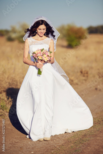 Beautiful smiling bride wearing a natural flower wreath and standing in the golden summer fields photo