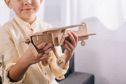 cropped shot of little boy holding wooden toy plane at home