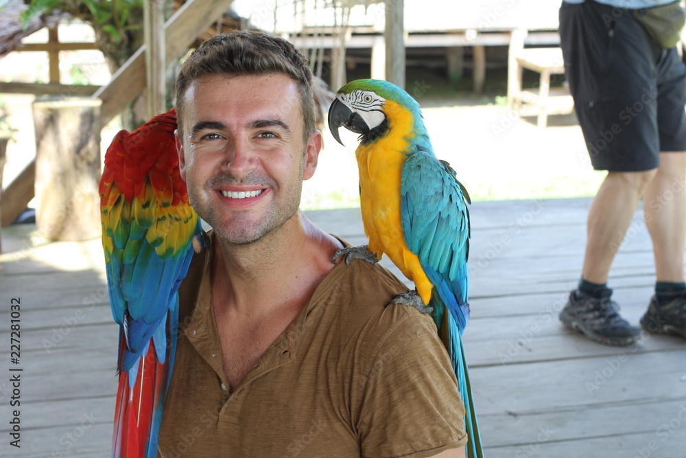 Naklejka premium Handsome man interacting with two gorgeous macaws