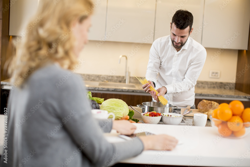 Man preparing a meal while a young woman sitting and use of tablets in a modern kitchen Man preparing a meal while a young woman sitting and use of tablets in a modern kitchen