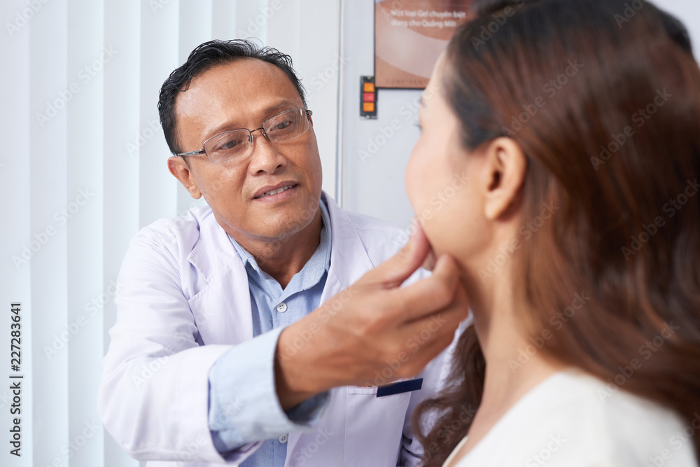 Confident Asian surgeon examining the face of his female patient and consulting her about operation Confident Asian surgeon examining the face of his female patient and consulting her about operation