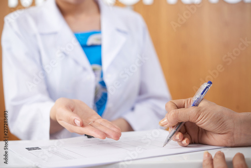Close-up of female hands filling medical documents at hospital with nurse in the background