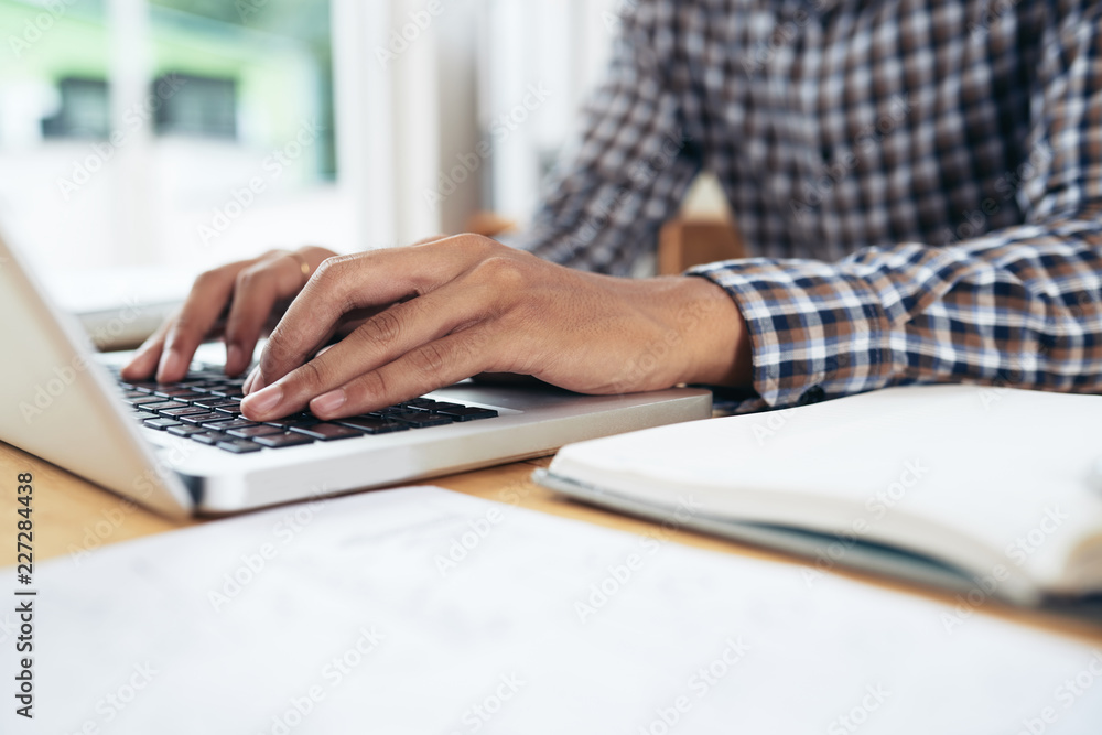 Fototapeta premium Close-up view of anonymous man in checked shirt sitting at table and typing on notebook