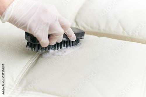 A woman cleans the leather sofa with a brush and detergent.