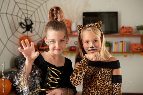 Portrait of beautiful Caucasian girls with painted faces fooling in smart Halloween dresses and smiling at camera joyfully