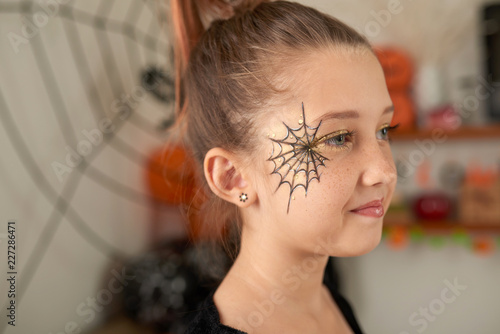 Half-turned portrait of little pretty Caucasian girl with makeup and  painted Halloween spider web on her face looking away and smiling Stock  Photo | Adobe Stock