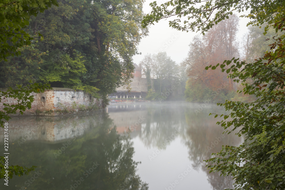 View through bushes over mist-covered water on the city wall of the city Augsburg with the moat at the oblatter wall