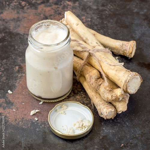 Foto Fresh horseradish roots and a small glass jar with seasoning on a dark background