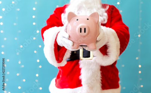 Santa holding a piggy bank on a shiny light blue background