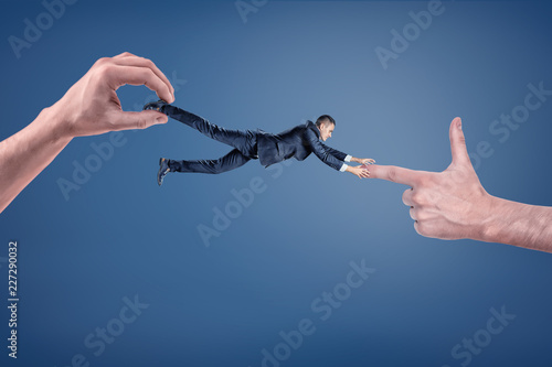 Obraz na plátně A small businessman being dragged away by a giant hand while holding another hand with a gun gesture