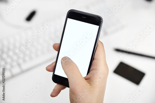 Hand holding a white blank screen smartphone over the desk