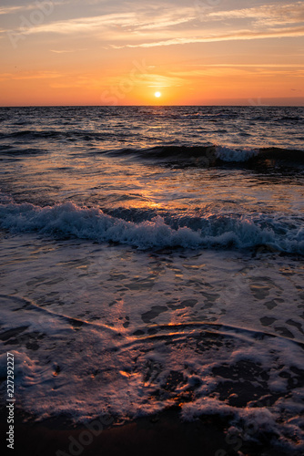 Sunrise and a beautiful cloudy sky early in the morning on the sandy shore on which the sea water beats and turns into foam