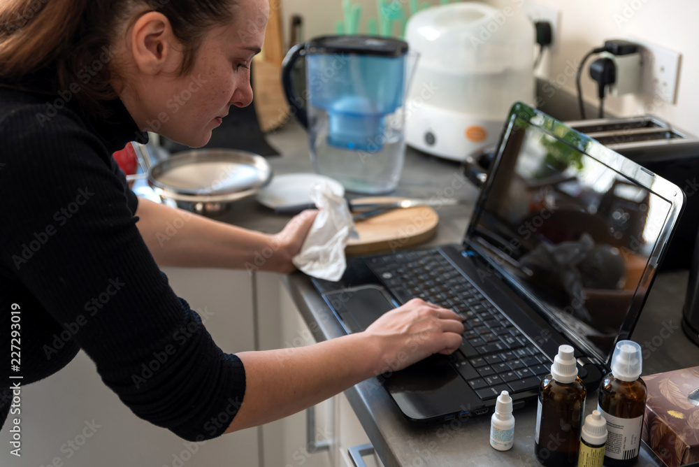 young sick woman working from home kitchen on laptop next to medicines
