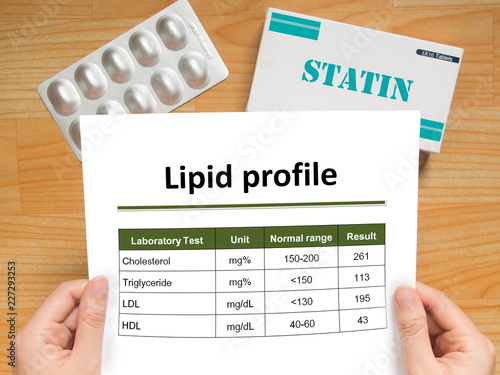 Physician checking blood laboratory results of lipid profile in high cholesterol patient and generic pack of statins tablets for treatment dyslipidemia on wood table. Health care and medical concept. photo