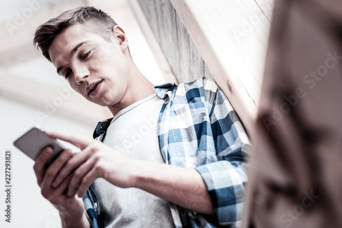 Important messages. Calm handsome young man chatting with his girlfriend and thoughtfully looking at the screen of a smartphone